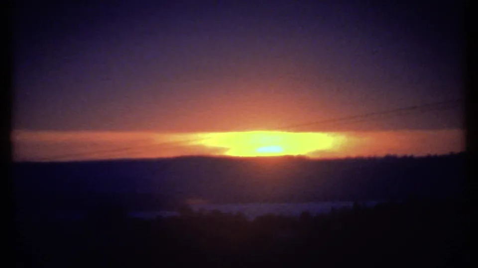 1979 8mm home-movie frame likely near Ithaca, showing a bright sunset over dark hills beneath a purple-blue sky.