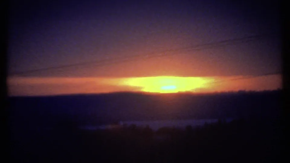 Vintage 8mm frame from 1979 likely near Ithaca, showing the sun partly lowered behind a dark ridge line.