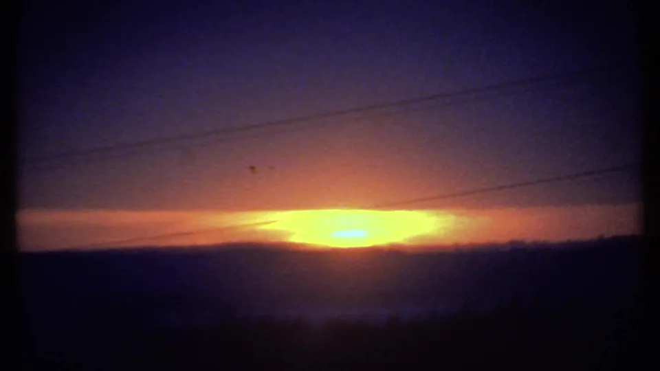 1979 8mm home-movie frame likely near Ithaca, with a low orange sun behind hills and utility wires crossing the sky.