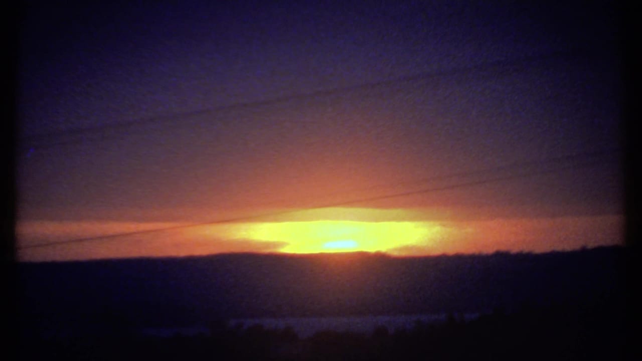 Low sunrise behind a dark horizon with orange sky and faint horizontal utility lines.