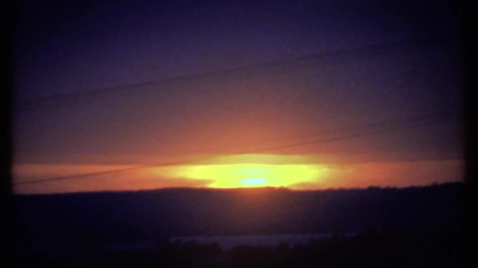 1979 8mm home-movie frame from the Ithaca, New York area showing a glowing sunrise behind a dark horizon and thin utility lines.