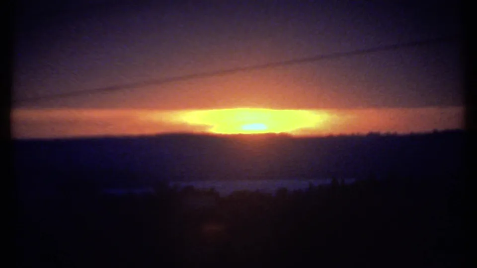 1979 8mm frame likely from Ithaca, New York, with the sun low under a dark cloud band above a silhouetted landscape.