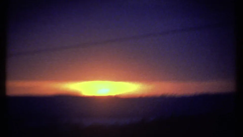 1979 8mm home-movie frame showing an elongated sunrise over the dark Ithaca-area horizon with saturated orange and yellow light.