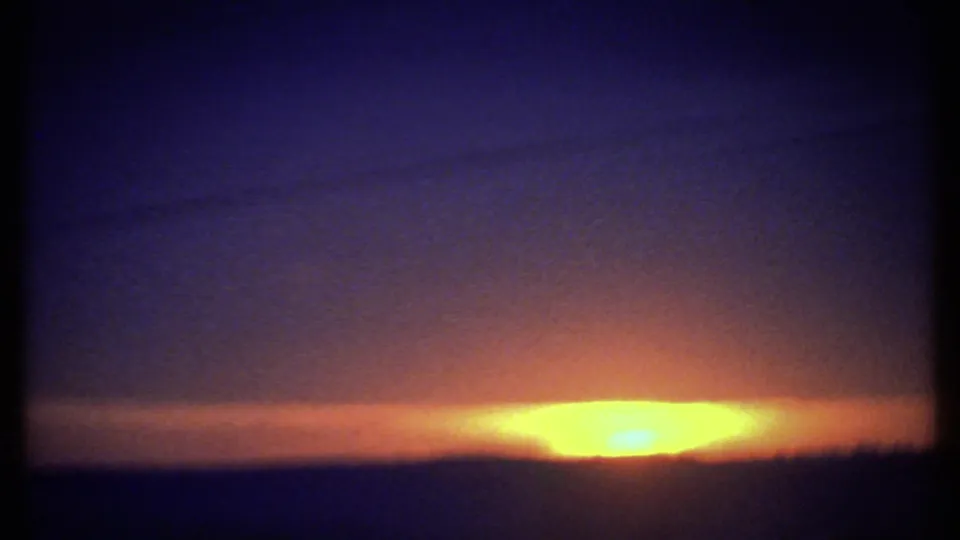 1979 8mm frame likely near Ithaca, New York, with a low sunrise at frame right, dark horizon, and blue-purple shadow in the sky.