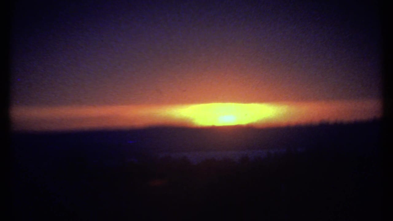 1979 8mm Ithaca sunset view with a wide orange glow under dark clouds and a nearly black hillside silhouette below.