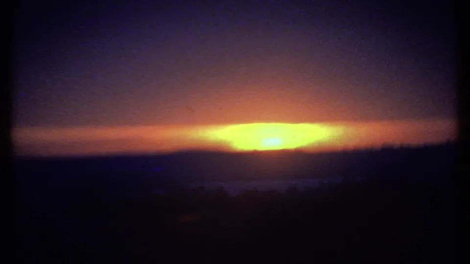 1979 8mm Ithaca sunset view with a wide orange glow under dark clouds and a nearly black hillside silhouette below.