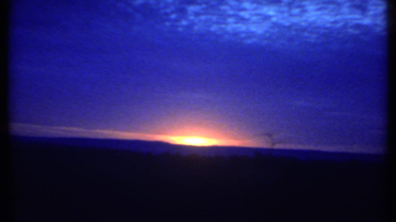 Low orange sunrise beneath a deep blue clouded sky and dark horizon.