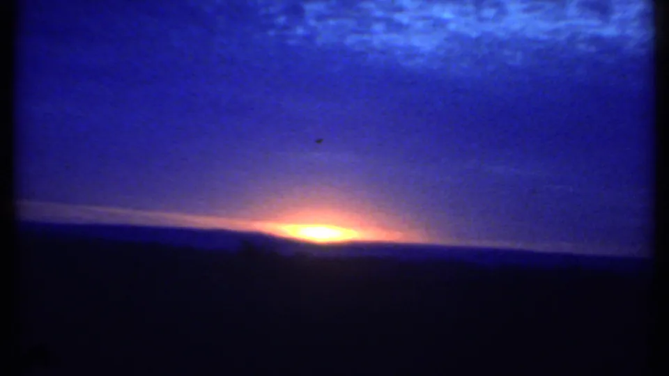 A dawn horizon in Ithaca, New York appears with orange light, blue clouds, and a small distant speck that may be a bird.