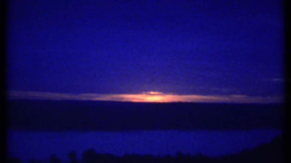 1979 8mm frame likely near Ithaca, New York, with a narrow orange sunset line beneath clouds and dark land silhouettes.