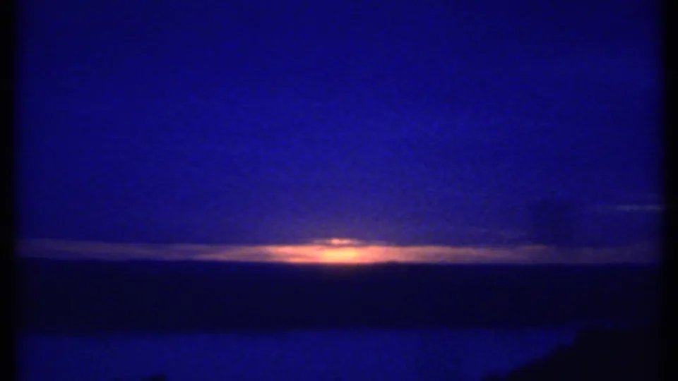 1979 8mm frame likely near Ithaca, New York, showing a soft sunset glow near the horizon above dark blue water or land.