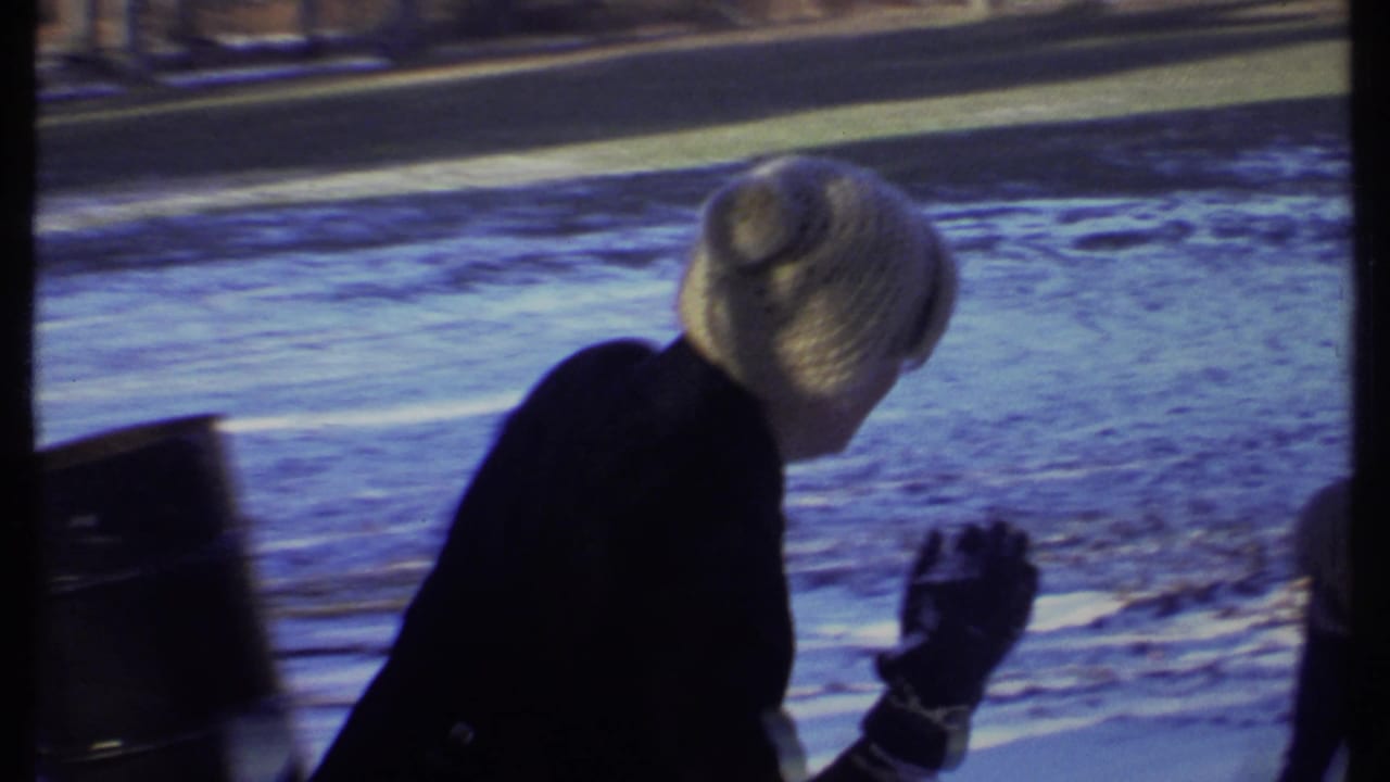 Person in knit hat raises a gloved hand beside snowy ground.