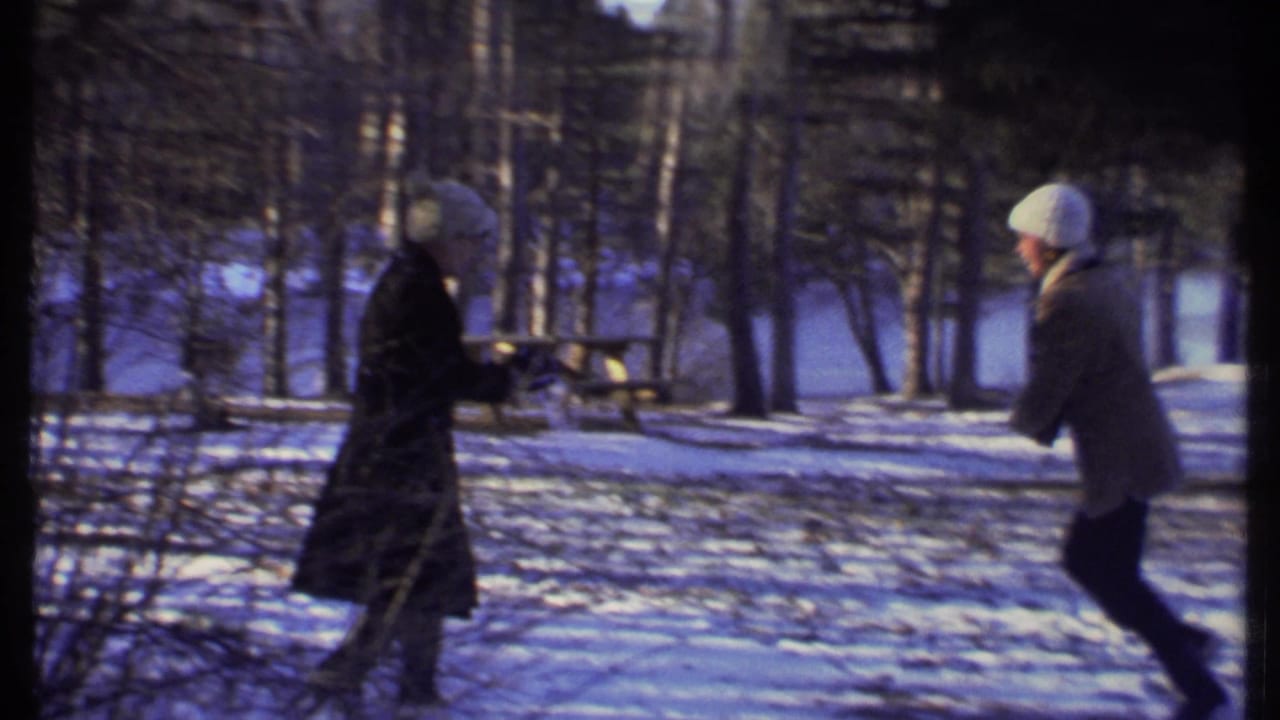 Two people in coats and knit hats face off in a snowy Ithaca park near a picnic table during the 1979 home-movie snowball fight.