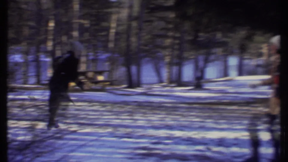 A bundled figure runs across the snowy park in 1979 Ithaca as another person remains partly visible at the right edge of the frame.