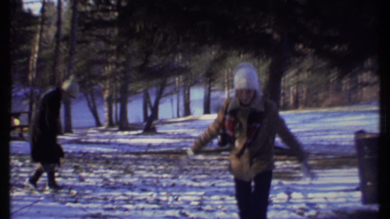 Two bundled teenagers in a snowy park, one moving forward with arms out.