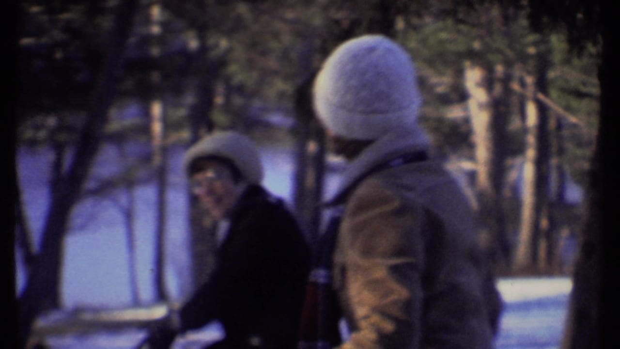 Two teenagers in knit hats stand close together in a snowy wooded area.