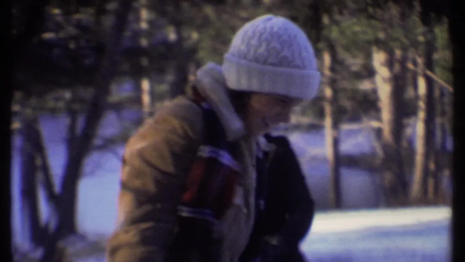 A bundled teenager in a white knit hat and tan coat bends forward in a snowy Ithaca park scene from 1979.