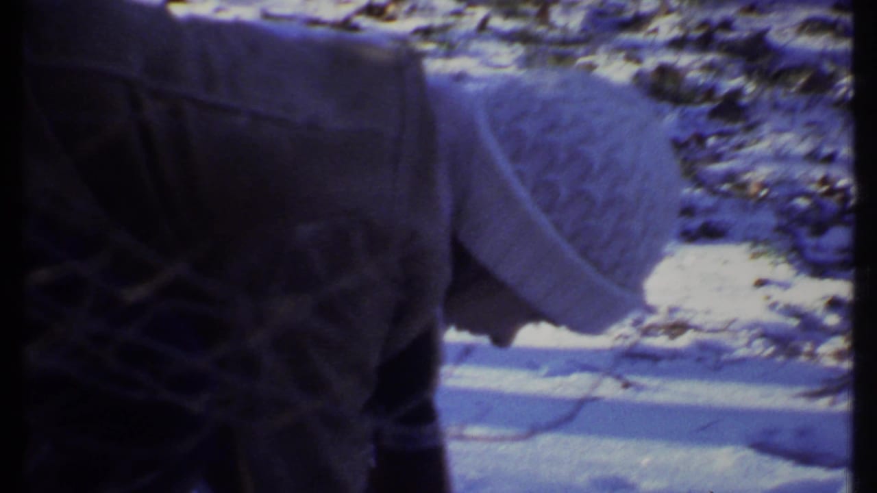 Person bending near snow-covered ground and bare trees in a winter outdoor setting.