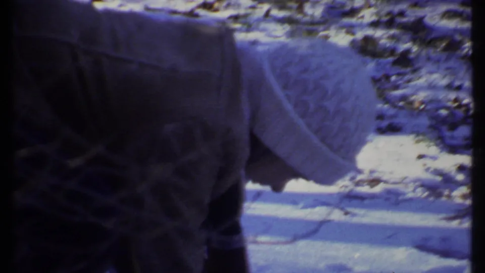1979 8mm home-movie frame from Ithaca showing a person bent over near snow and bare trees in a wooded winter area.