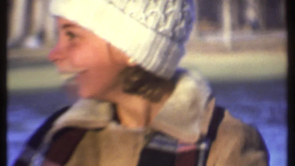 A person in a white knit hat and shearling-style winter coat smiles in profile during the 1979 Ithaca snow scene.