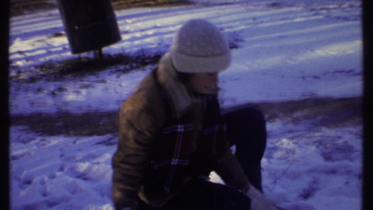Woman in a white knit hat crouches in snow beside a dark vertical object.