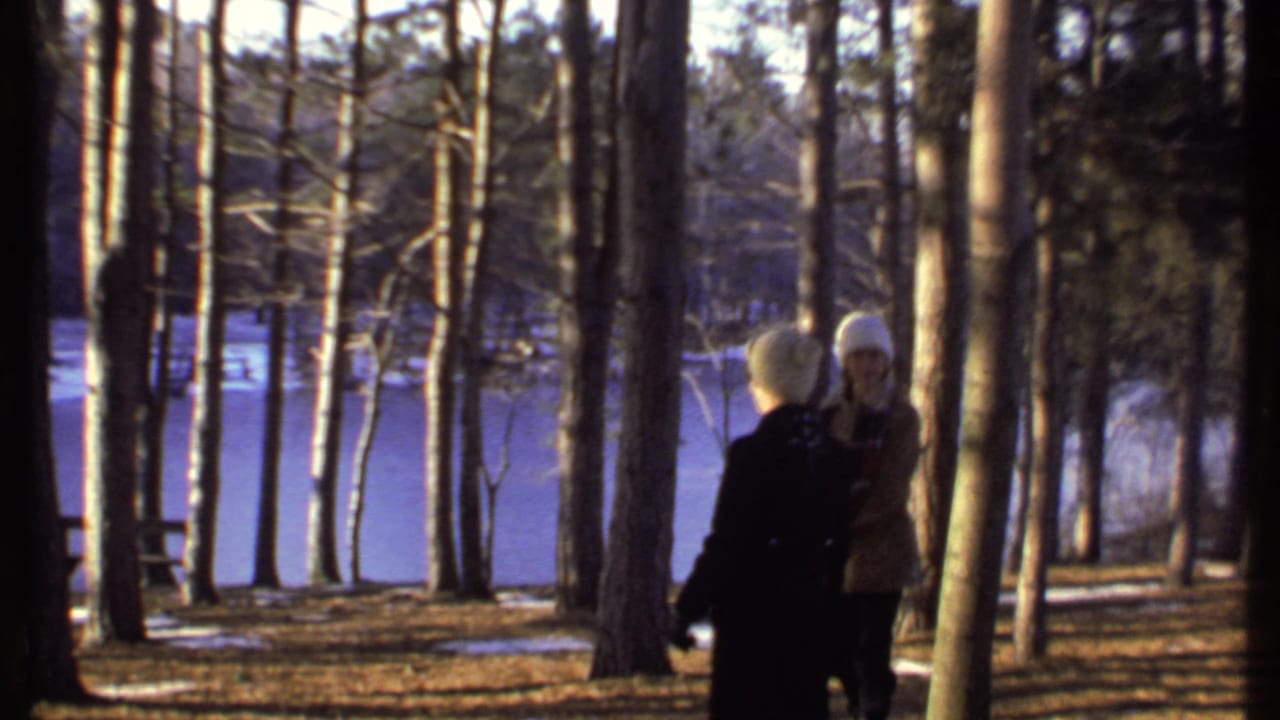Two bundled-up people stand in a wooded area near a frozen lake in Ithaca, New York, in 1979 home-movie footage.