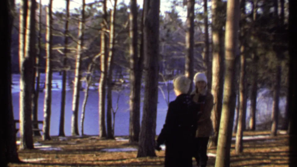 Two bundled-up people stand in a wooded area near a frozen lake in Ithaca, New York, in 1979 home-movie footage.