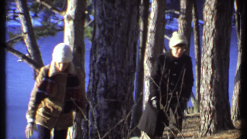 Final 1979 home-movie frame shows two winter-dressed adults walking through wooded lakeside terrain in Ithaca.