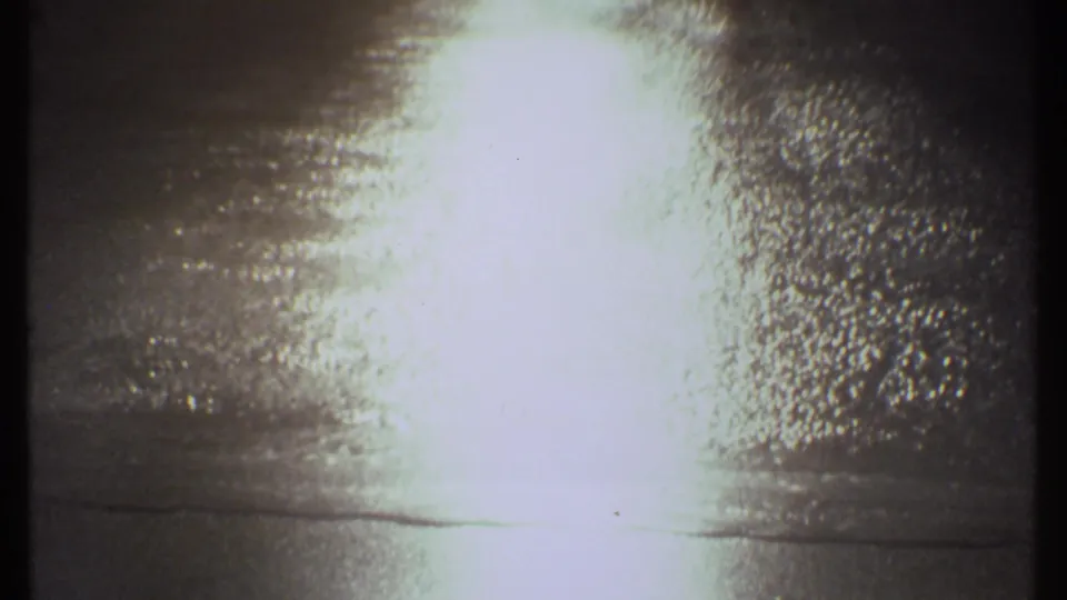 The frame holds on bright reflected sunlight over rippled lake water, with 8mm exposure bloom and a dark gate edge.