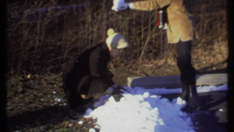 Two people in winter clothing play beside patchy snow and bare brush in a short 8mm Ithaca, New York scene from 1979.