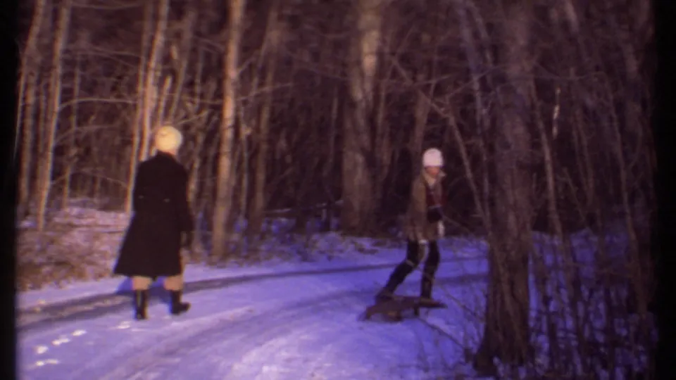 Two bundled figures appear on a snow-covered path through bare trees in 1979 Ithaca home-movie footage.