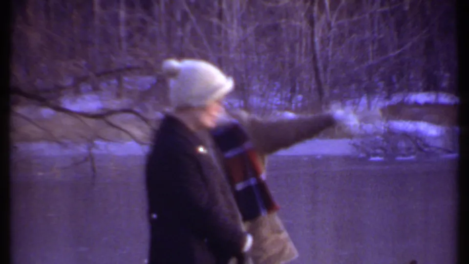 In Ithaca, New York home-movie footage from 1979, two bundled people stand near a frozen pond as one gestures toward ducks on the ice.