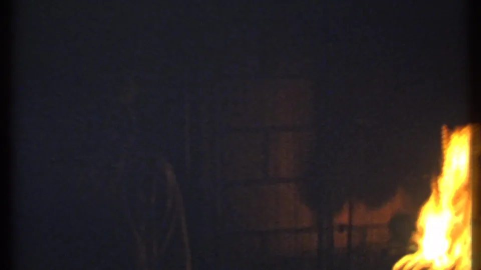 A dark 8mm frame shifts to firelight, with bright flames flickering against a mostly shadowed background.