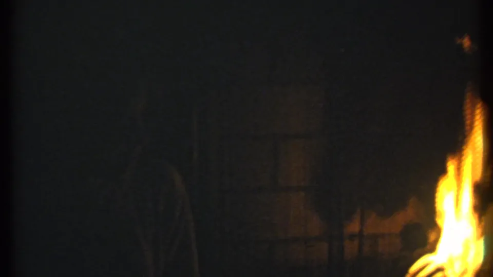 The final frame holds on bright firelight at the edge of a dark scene, with warm flare and heavy shadow detail.