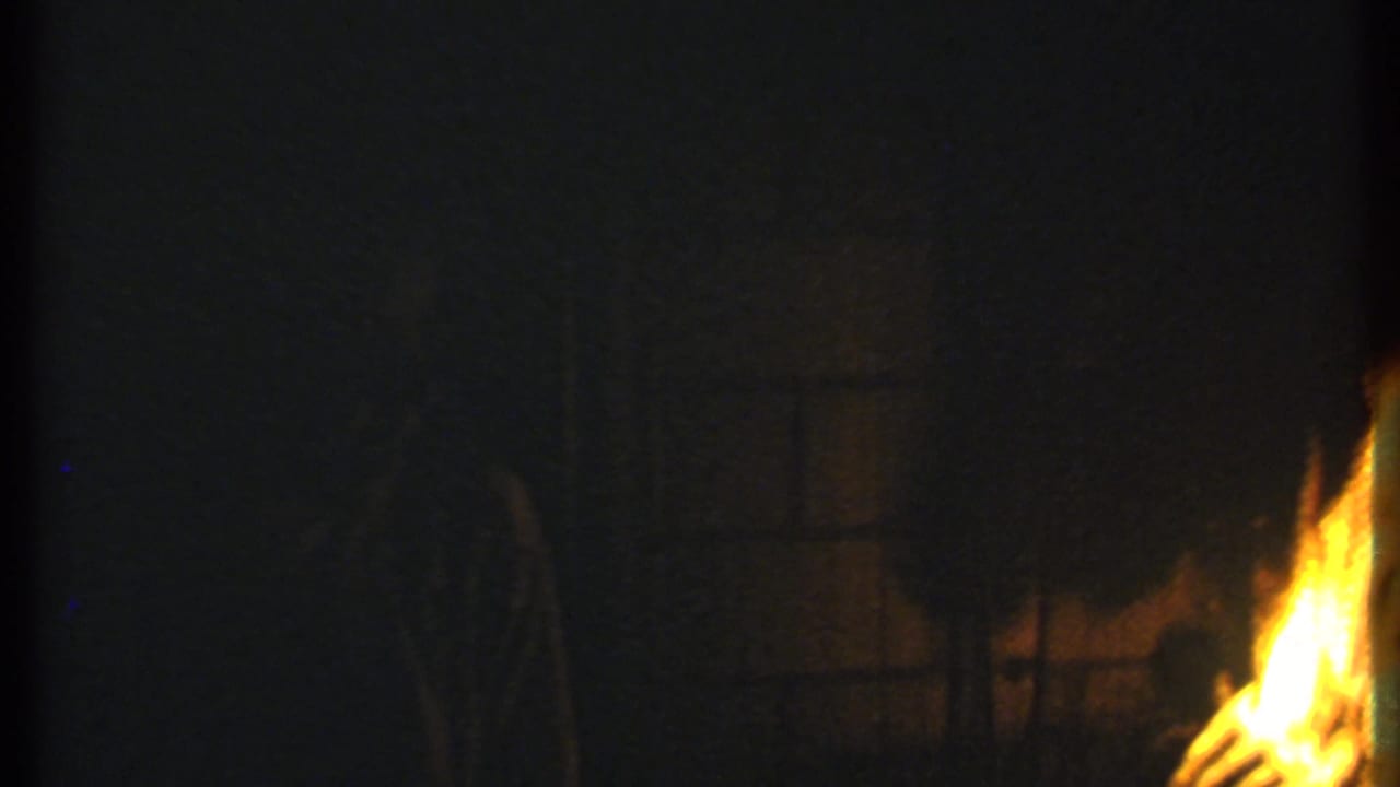 Large flames burn at night beside dark silhouettes and shadowed outdoor shapes.