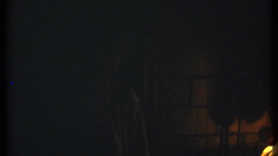 Dark 1979 Ithaca home-movie frame with a partial fire glow and barely visible figures or brush forms.