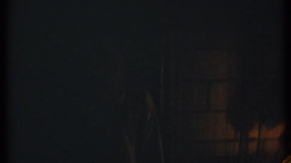 Low-light 8mm frame from Ithaca in 1979 with faint fire glow and unclear figures in shadow.