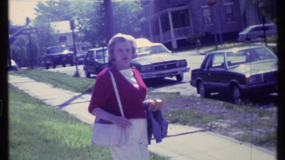 A woman in red and white clothing faces the camera in a suburban street scene from the supplied 1984 Vermont clip.