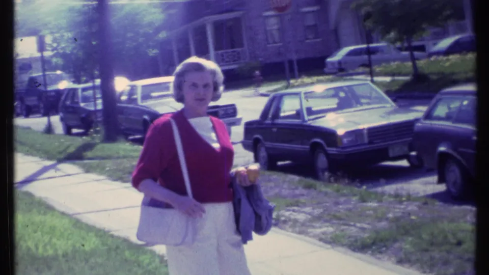 The closing frame shows the woman facing the camera in a residential street setting with cars, lawns, trees, and houses.