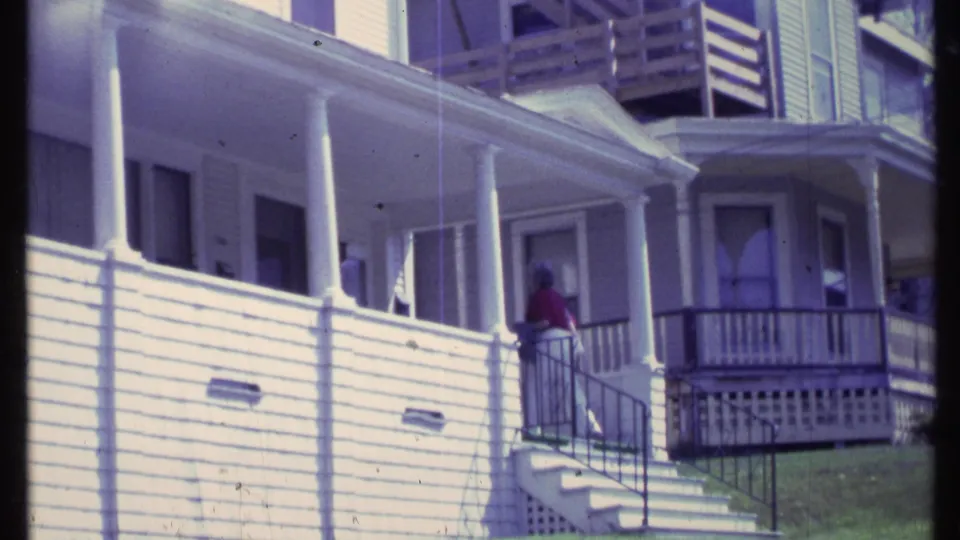 The woman continues along the front steps and railing of the white clapboard house in Vermont home-movie footage.