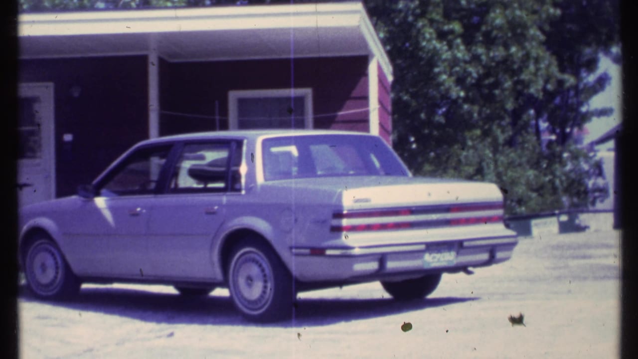 Light-colored sedan parked in front of a red-sided house with a white porch.