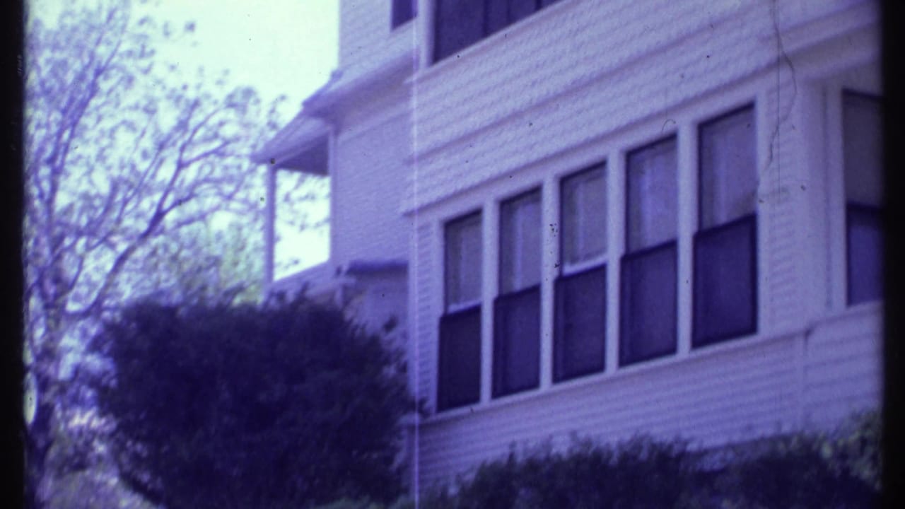 White house facade with several windows, bushes, and trees in soft focus.