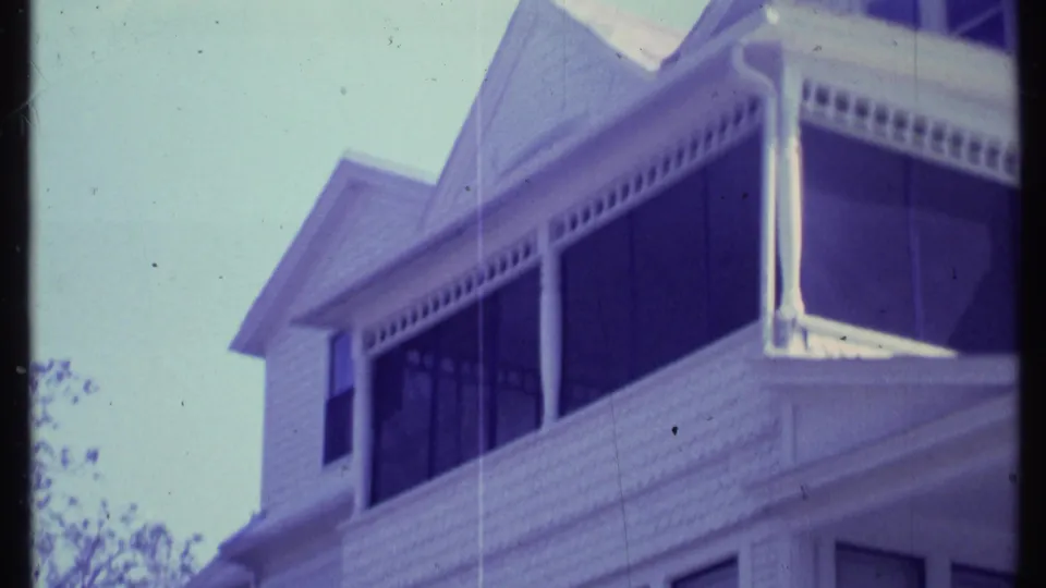 1984 Vermont 8mm frame showing a close handheld view of a white house porch, columns, screened windows, and upper roofline.
