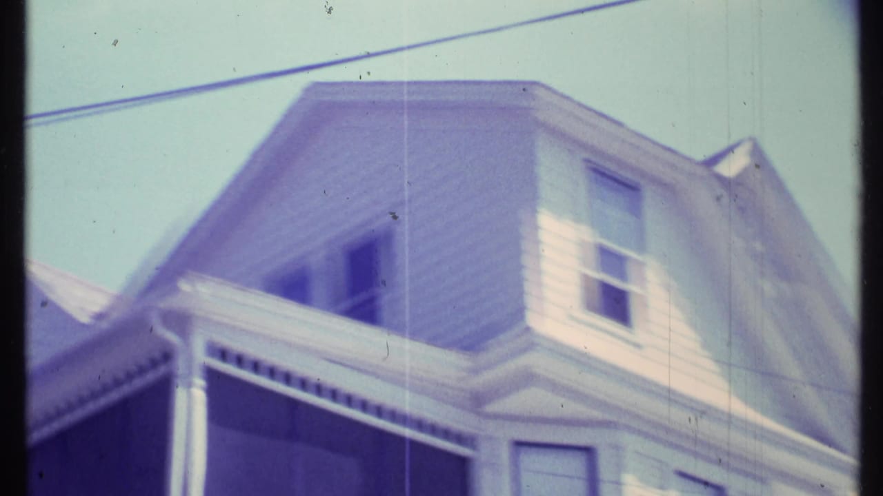 1984 Vermont 8mm frame showing the top half of a white clapboard house with a gabled roof, windows, and decorative porch trim.