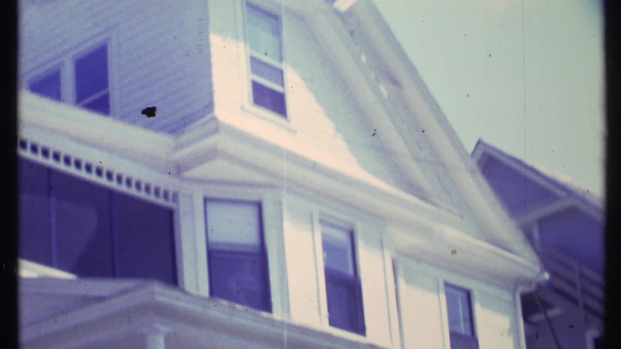 White house facade with gable, windows, and shaded porch area.