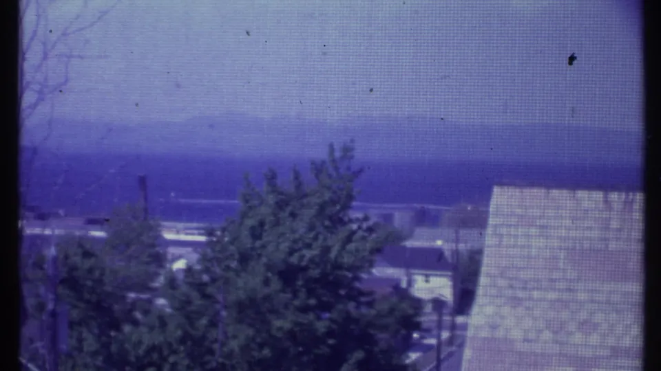 1984 Vermont 8mm frame showing a screened view over leafy trees and a sloped roof toward hazy distant mountains.