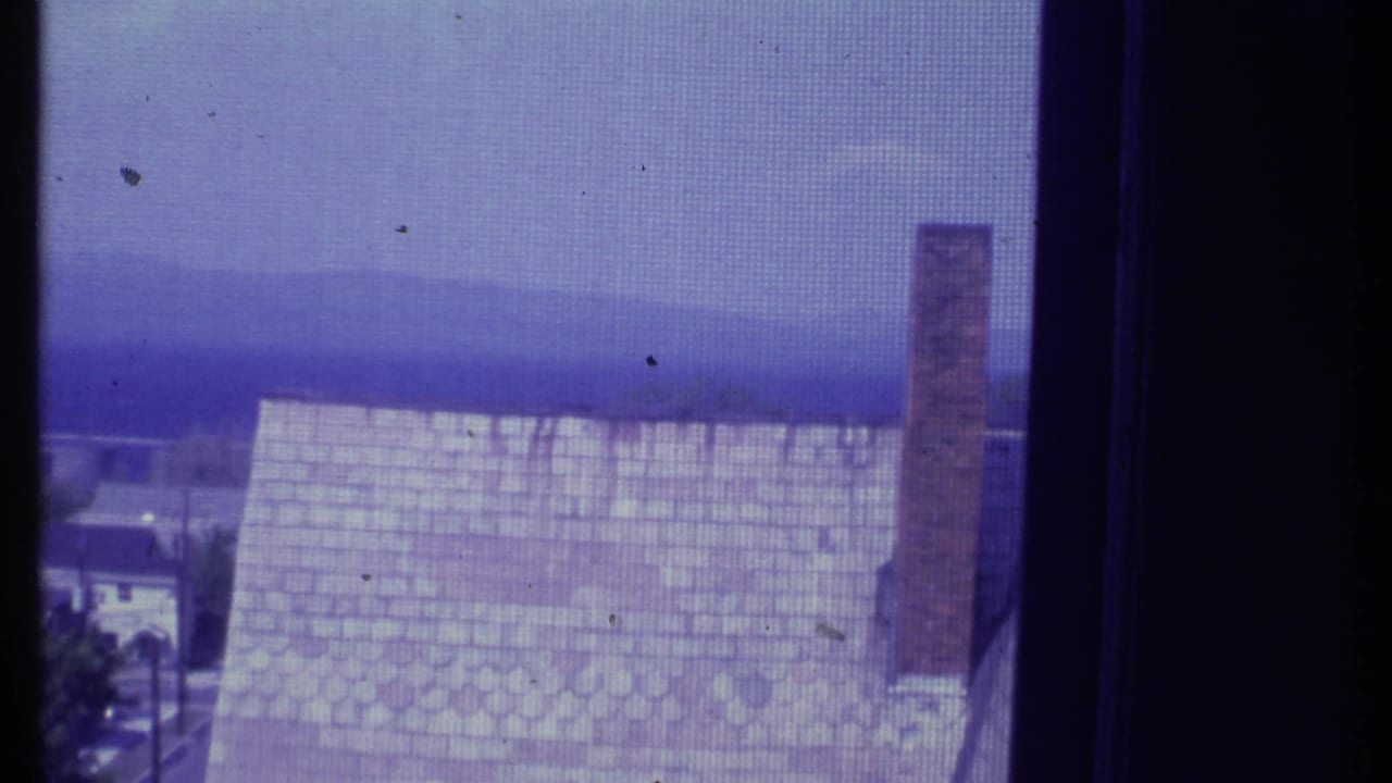 Roofline and chimney seen through a window or screen with distant landscape beyond.