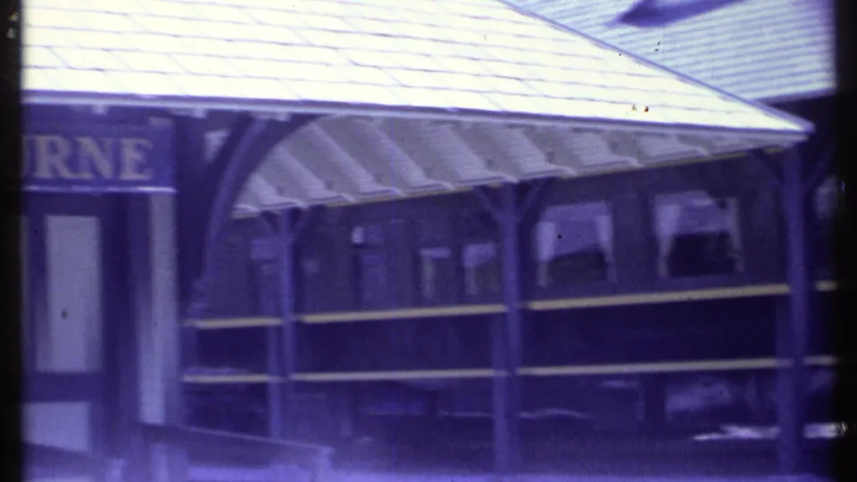 The station view shifts along the platform, showing a partially cropped SHELBURNE sign, canopy supports, roofline, and train windows.