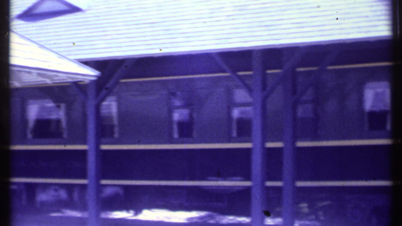 Covered platform and side windows of a dark train car, partly divided by a vertical film or frame edge.