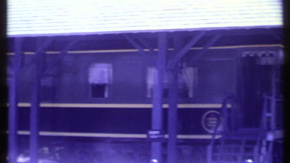 1984 Vermont 8mm frame of a passenger car doorway or cab section under a covered platform, with steps, posts, and soft motion blur.