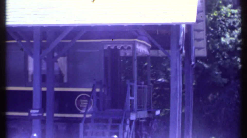 Final 1984 Vermont 8mm frame showing the end area of a dark passenger car, covered platform structure, steps, and nearby greenery.